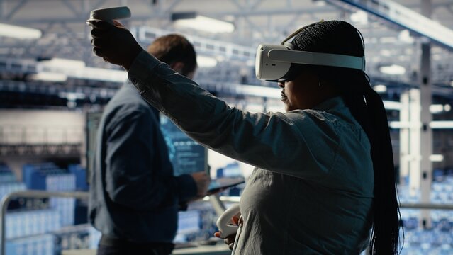 Software developer in server room wearing VR goggles optimizing deep learning systems handling tasks. African american woman in data center adjusts AI model parameters using virtual reality, camera B