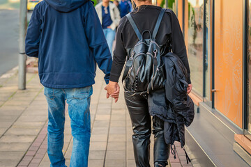 Young couple walks hand in hand on sidewalk, dressed in casual streetwear and leather. Concept of love, relationship, urban romance, casual urban lifestyle