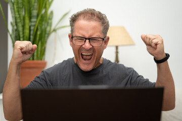 Excited man cheering for victory achieving goal with laptop