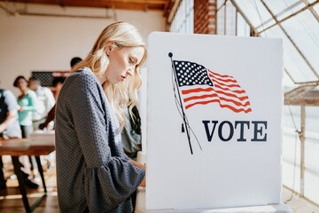 A woman voting at a polling station. The woman is casting vote. The voting booth has an American...