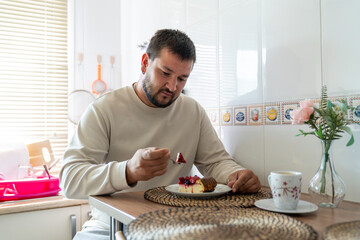 Man enjoying snack in kitchen, having cheesecake with berry topping and coffee for breakfast