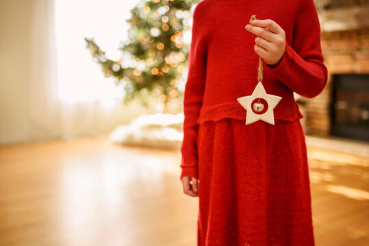 Close-up of a Girl in a red dress standing front of a Christmas tree in a living room holding a star shaped Christmas ornament