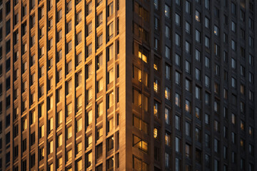 Sunlit corner of a modern high-rise office building with golden evening reflections on repetitive windows creating warm geometric patterns