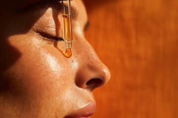 Golden facial serum droplet falling from glass dropper on close-up woman's skin — skincare beauty hydration and natural glow concept