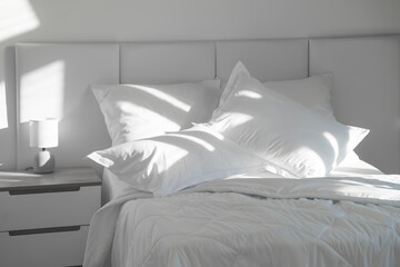 A bed with white pillows and a blanket, next to a bedside table with a lamp, daylight