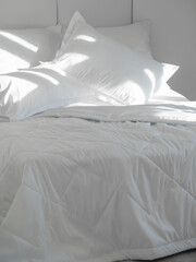 A bed with white pillows and a blanket, next to a bedside table with a lamp, daylight