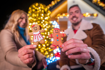 Couple holding gingerbread cookies in front of Christmas lights
