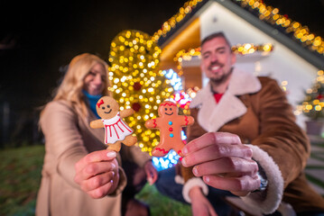 Couple holding gingerbread cookies in front of a Christmas tree at night
