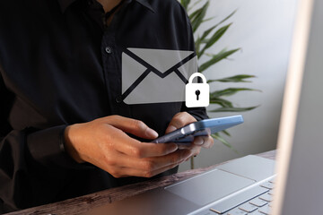 Email security. A businesswoman working on her computer, holding a mobile phone, with an icon of an...