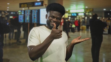 Man giving thumbs up and presenting open palm at busy airport terminal while smiling; friendly confidence.