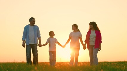 Family relaxation on lawn. Happy family, dad mon daughters strolling at sunset summer park. Parents children enjoying summer walk in nature. Dad mom daughters, holding hands, outdoors. Family unity