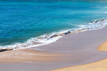 Scenic view of pristine beach with turquoise water gently lapping against golden sand. Calm waves create peaceful atmosphere on sunny summer day