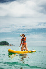 Woman paddling on yellow stand up paddleboard in turquoise sea under blue sky. Concept of active...