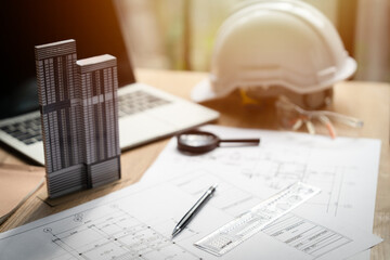 A laptop and a model of a building are on a table. The laptop is open and the model is on top of it. A magnifying glass is also on the table