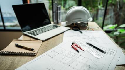 A laptop is on a desk with a drawing of a building and a set of drafting tools. The drawing is of a building with a large window and a balcony. The drafting tools include a ruler, a pencil, and a pen