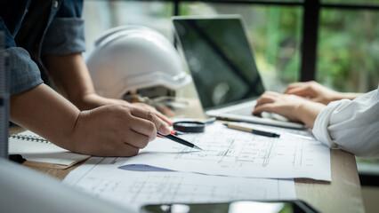 A group of people are working on a project, with one person holding a pencil and pointing at a drawing. The atmosphere seems to be focused and collaborative
