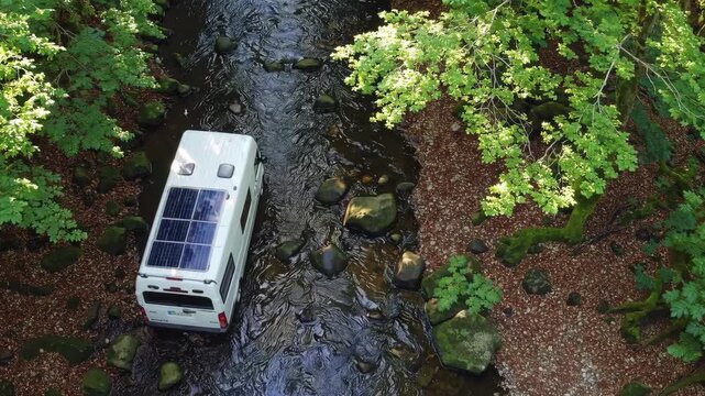 Camper van with solar panel parked by forest creek, surrounded by lush green trees and rocks, peaceful nature outdoor adventure escape tranquil