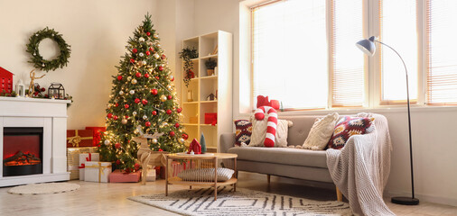 Beautiful decorated Christmas tree, fireplace and sofa in interior of living room