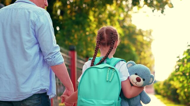 Father little daughter schoolgirl, walk to school with backpack, child holding teddy bear. Parent father, child girl, walk together outdoors. Children's education concept. Happy family walk in park