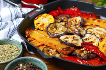 Tasty grilled vegetables in pan and spices on wooden table, closeup