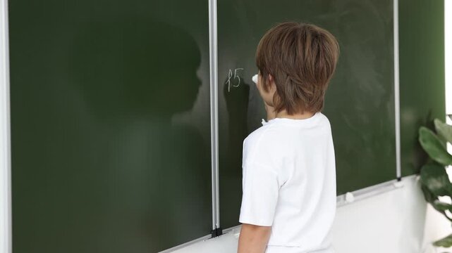 Back to school. Boy doing math on chalkboard indoors