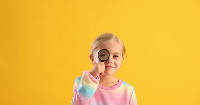 Cute girl looking around through magnifying glass on yellow background