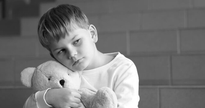 Upset little boy with toy bear on stairs indoors, black and white effect