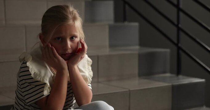 Sad little girl crying on stairs indoors, space for text