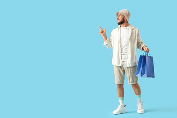 Stylish young man with shopping bags pointing at something on blue background