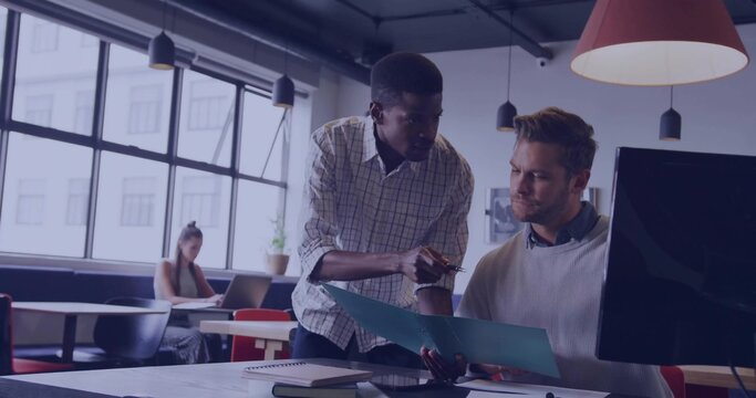 Leaning male co-workers pointing at blue folder on wooden desk in open-plan office, with pen - Powered by Adobe