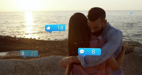 Hugging couple sharing sunset at rocky sandy beach, with thumbs-up, follower and comment icons