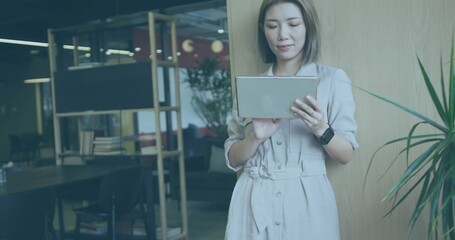 Holding tablet Asian woman leaning against partition in office, with shelving, copy space