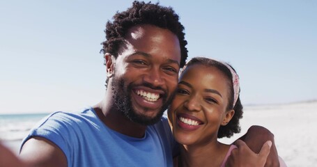 Smiling African American couple taking selfie on beach shore, with smartphone and casual clothes