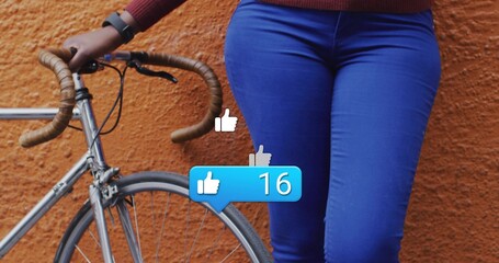 Posing woman at orange wall holding drop handlebars of bike with thumbs-up notification showing 16
