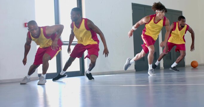 Performing defensive slide drill basketball players in yellow-red jerseys at gym, with basketball