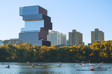 A group of unrecognizable rowers on the Charles River with Boston’s modern skyline and autumn...