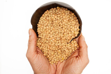 Top view of hands holding lentil seeds in black plate on white background