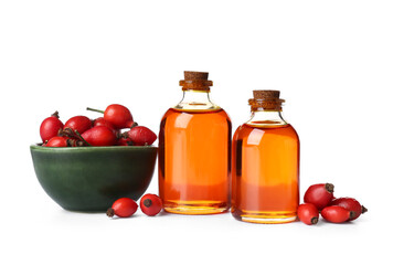 Bottles of cosmetic rose hip oil and bowl with berries on white background