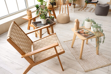 Interior of light room with wooden armchair, tables and green plants