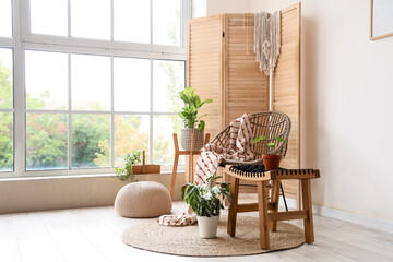 Interior of light room with wicker armchair, folding screen and plants