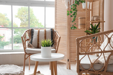 Interior of light room with wicker armchairs, wooden folding screen and plants