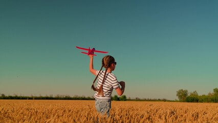 Happy girl runs with toy airplane through wheat field. Little girl plays with toy plane, dream fly. Child aviator dreams of flying travel. Child dreams of soaring into sky becoming pilot. Slow motion
