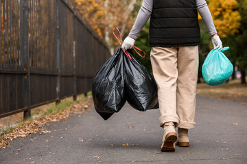 Woman with garbage bags walking on street, back view