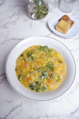 A traditional Indonesian meal featuring Bubur Manado or porridge with vegetables and salted fish on a classic plate, accompanied by fried tofu and a glass of water. A top view of traditional Bubur Man