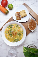 Bubur Manado or Tinutuan porridge. Indonesian food - Manado traditional rice porridge, mixed with pumpkin, corn, vegetables. Served with salted fish and sambal or chili sauce