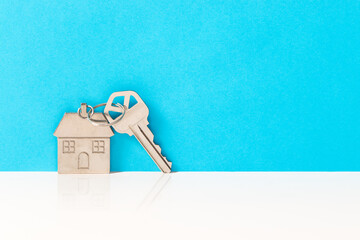 A silver key with house shaped keychain against a sky blue background, symbolizes new home ownership, real estate or mortgage loan