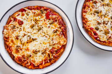 two small margherita pizzas with olives on bigger plates, portion control concept