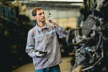 White man technician checking used car damaged engine block at scrap yard warehouse recycle area...