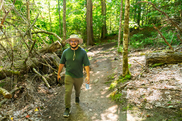 Relaxed hiker exploring nature trail with hat and water bottle in hand.