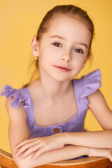 Beautiful girl in lavender dress poses on yellow background. 
Soft natural light highlights her gentle expression and charm.
Bright child portrait shows confidence, innocence, and style.